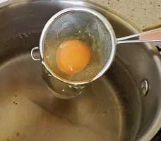 В чуть кипящую воду аккуратно опускаем яйцо с ситечка